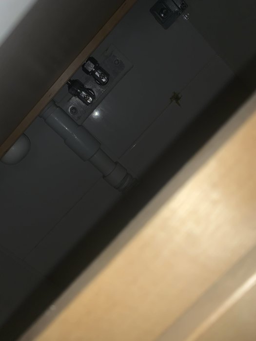 Vit avloppsslang som ansluter till ett skåp underifrån med närliggande ventiler.