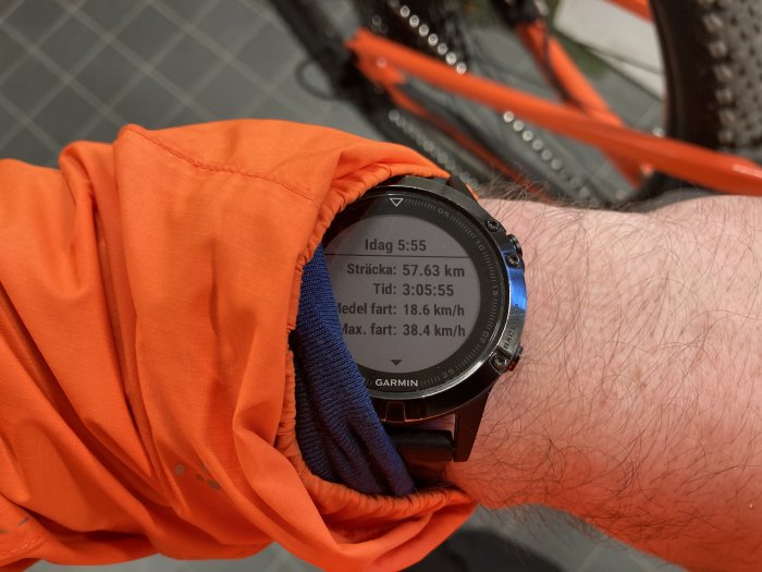 Person med en smartklocka som visar träningsdata med en cykel i bakgrunden.