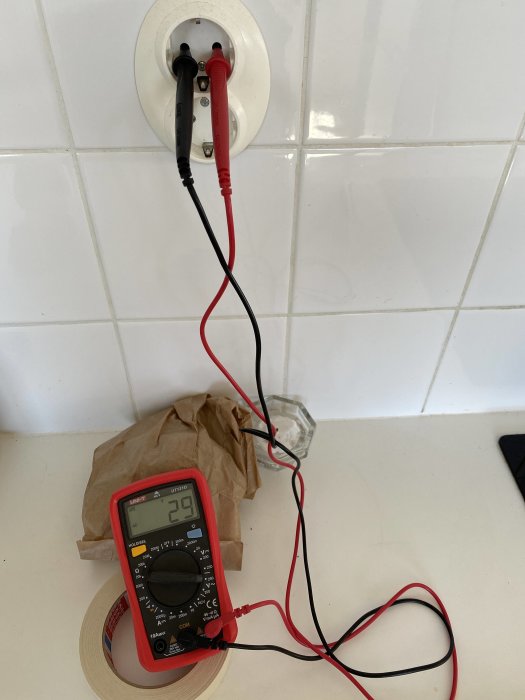 Multimeter som visar 29V ansluten till vägguttag, indikerar spänningsfall efter säkring slagit ifrån.