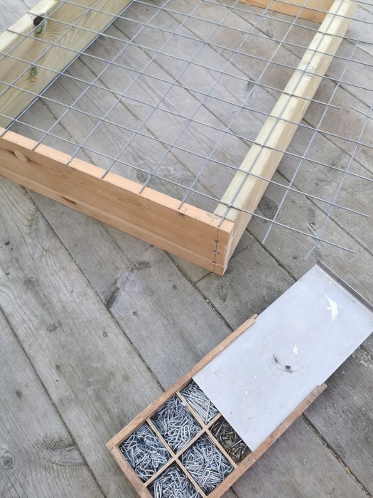Hemmagjort såll för skottkärra med träram och metallnät, bredvid en låda med märlor.