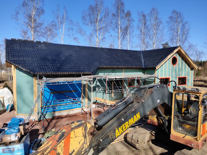 Nyinstallerade takpannor på en byggnad med byggställning och en grävmaskin i förgrunden.