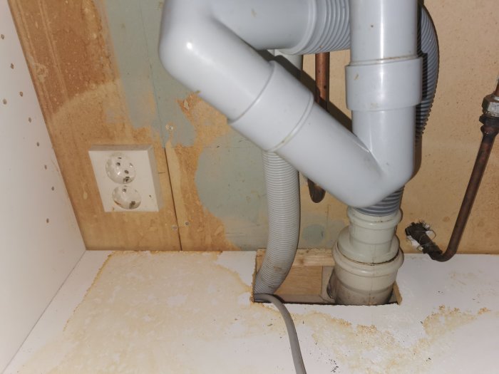 Under-sink plumbing with disconnected plug, hoses running through cabinet hole.