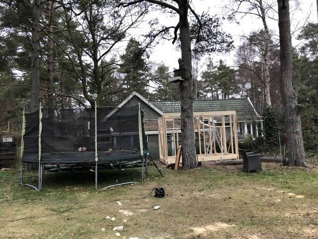 Byggställning av trä för ett husprojekt i en trädgård med trampolin och grönska.