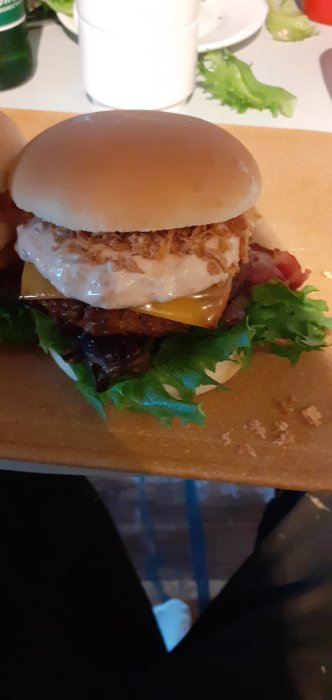 Hamburgare med bröd, ost, sallad, tomat och sås serverad på en träbräda.