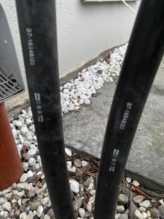 Tre svarta kablar sticker upp ur marken bredvid en vit husvägg och små vita stenar.