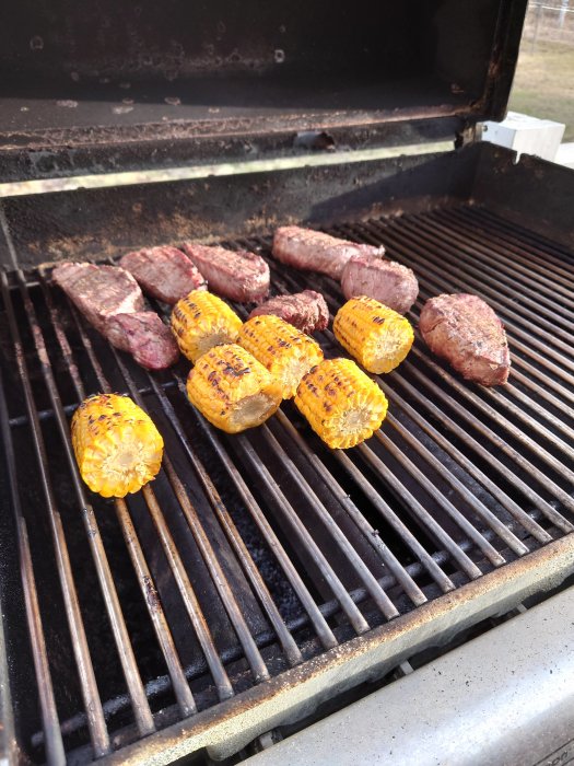 Grillat kött och majskolvar på en gasgrill.