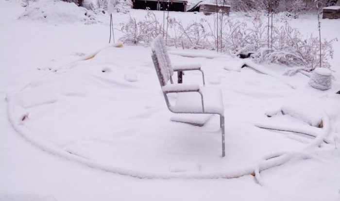 Trädgård under snö med synliga konturer av en tilltänkt rund uteplats markerad med gult plaströr.