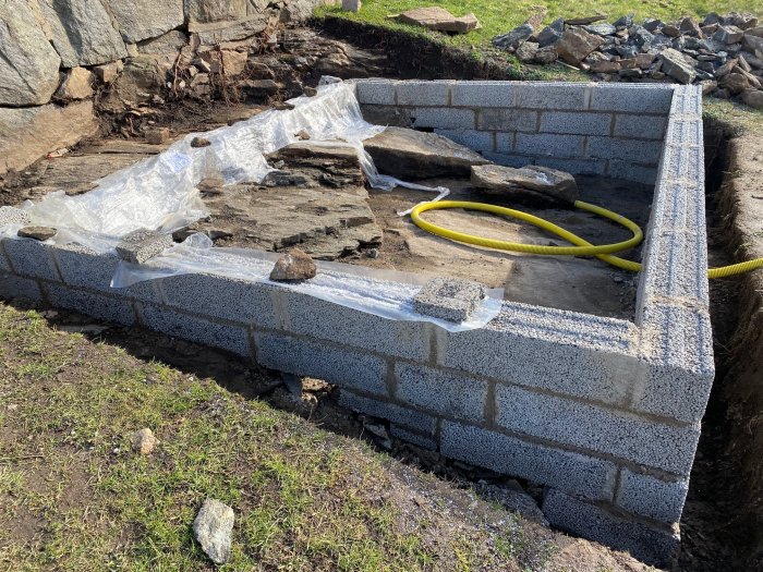 Nybyggd mur av lättbetongblock på sluttande bergsterräng, täckt med plast, med bekymmer för makadamtryck.
