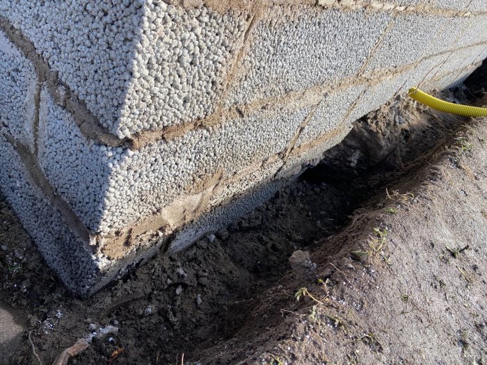 Nybyggd mur på berg i sluttande terräng, synlig bistål i fogar, beredd för makadamfyllning.