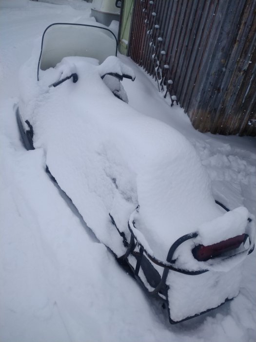 Bil täckt av snö med synliga sidbackspeglar och del av framlykta.