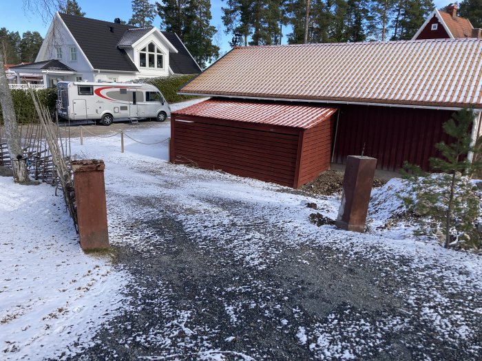 Två murade grindstolpar står snett på en uppfart med snöfläckar och bakgrund av hus och husbil.