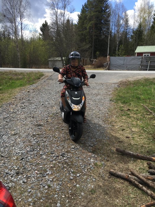 Moped parkerad på grusad infart med lätt sluttning och en synlig böj åt höger.
