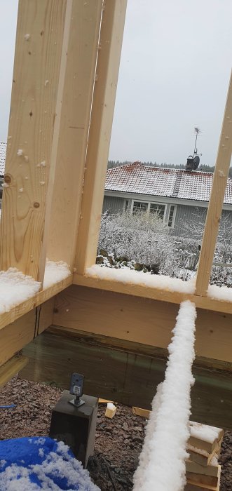 Dubblade träreglar i hörn av stomme för isolering, med snö och hus i bakgrunden.