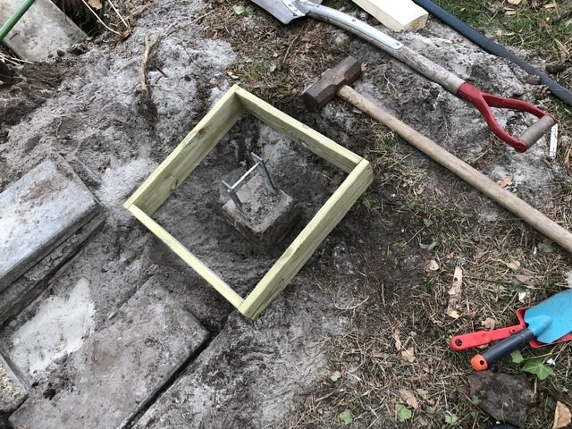 Förberedelse för gjutning av betongkrans runt en plint med verktyg och sandig mark.