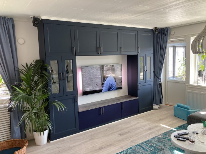 Ett vardagsrum med en mörkblå tv-bänk med inbyggd TV och textilfronter, omgiven av matchande skåp och hyllor.
