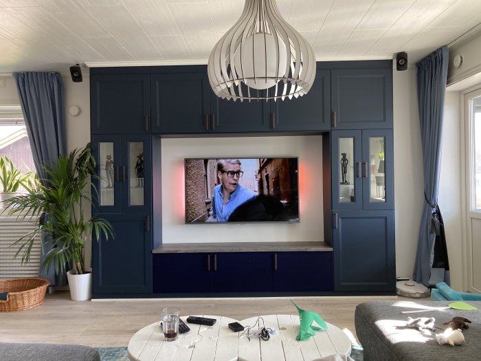 Tv-bänk integrerad med mörkblåa skåp runt TV:n och öppen lucka på en ljudanläggning, i ett vardagsrum.