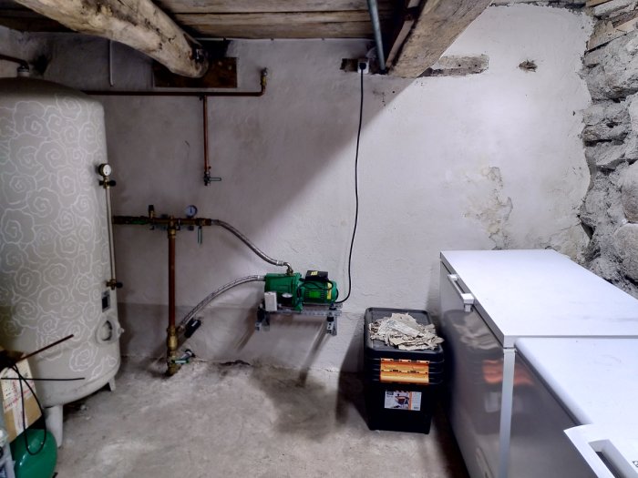Nyinstallerad pump med flexibel slang kopplad till vattenledningssystemet i ett källarrum.