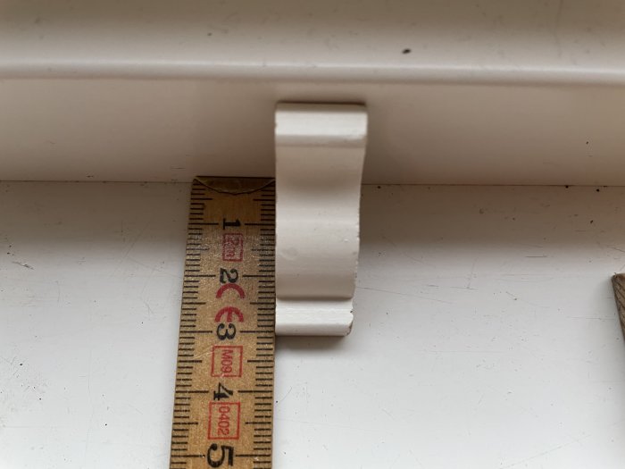 Vit golvsockel vid en vägg mätad med tumstocken, bredd cirka 93 mm.