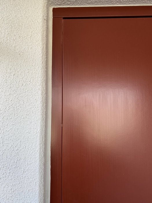 Brun ytterdörr som hänger snett och lämnar en ojämn klyfta vid karmens övre hörn.