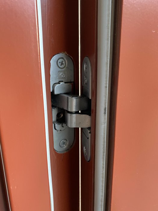 Närbild på en röd dörrs gångjärn som ser slitet ut, vilket indikerar att dörren kan hänga snett.