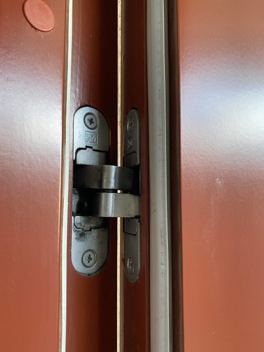 Slitet dörrgångjärn på en röd dörr som kan behöva justering för installation av Yale-lås.