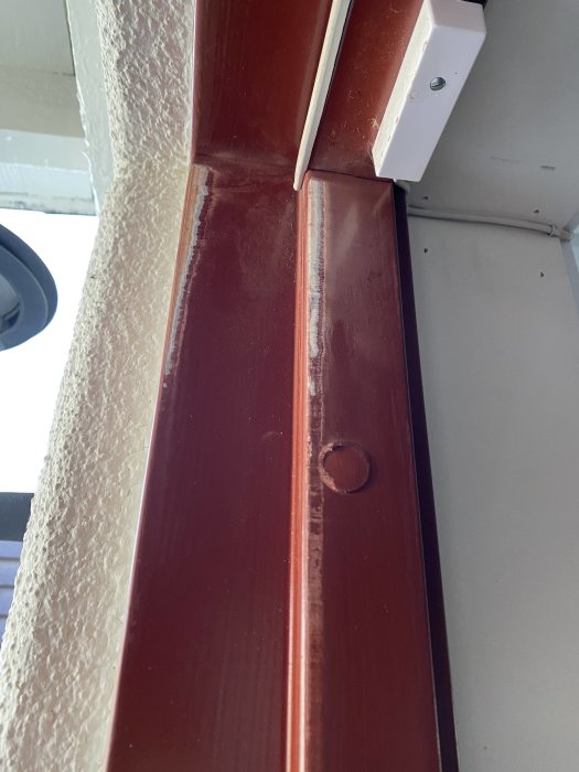 Närbild av en ytterdörrs övre gångjärn som verkar slitna eller feljusterade.