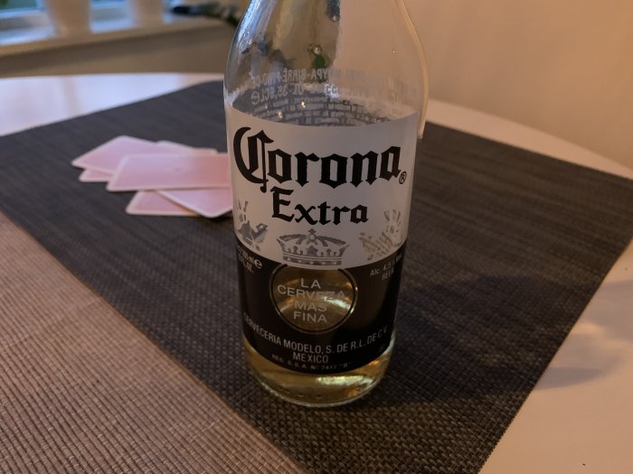 Tom flaska Corona Extra-öl på bord med spelkort i bakgrunden.