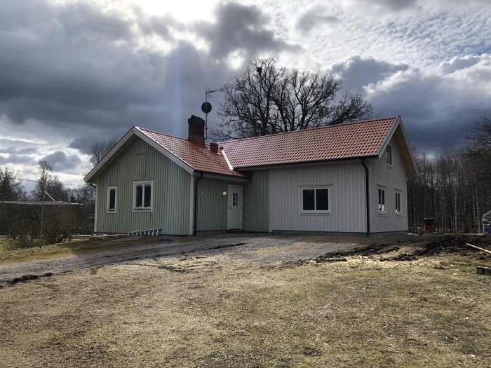 Renoverat hus med ljust träfasad, rött tak och ett pågående markarbete framför huset.