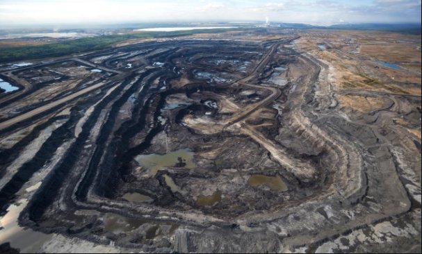 Aerial view of a vast, industrial oil sands extraction site with open pits and water bodies.