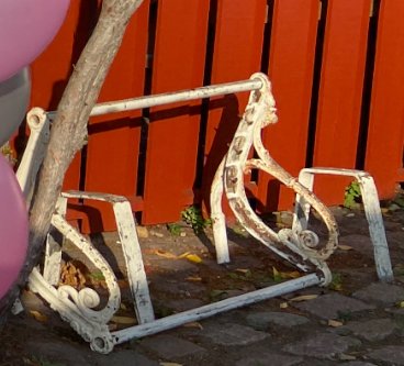 Gjutjärnssidorna av en gammal parkbänk utan träribbor mot en orange bakgrund.