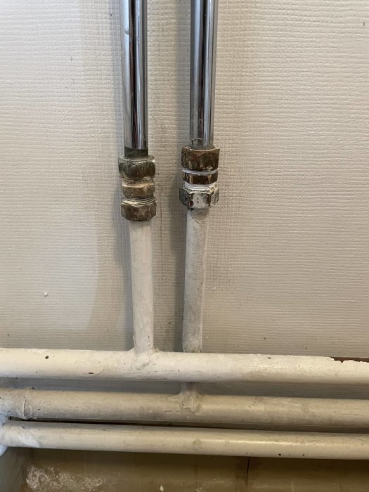 Gamla rörkopplingar på vägg ovanför ett vitmålat rörledningssystem.