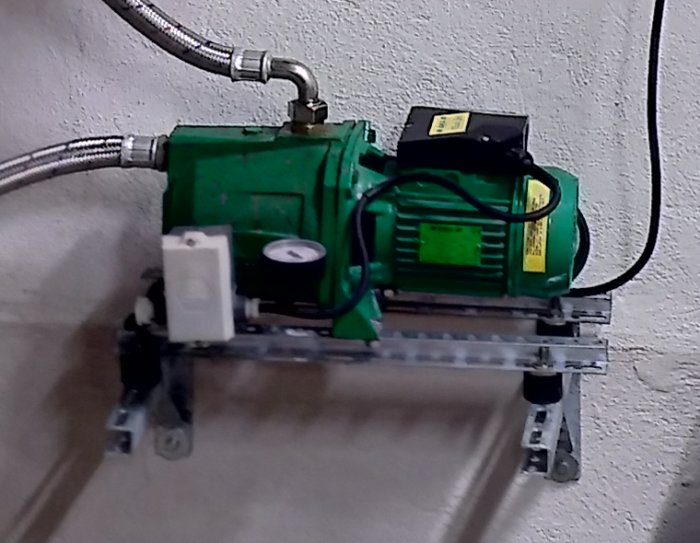 Grön pump monterad på skenor och gummikuddar fastbultade i betongvägg med slangar anslutna.