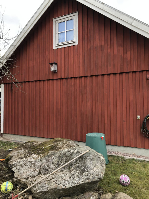 Rödfärgat hus med vitkant och fönster ovanför en stor bergsklump, potentiell plats för trappbygge.