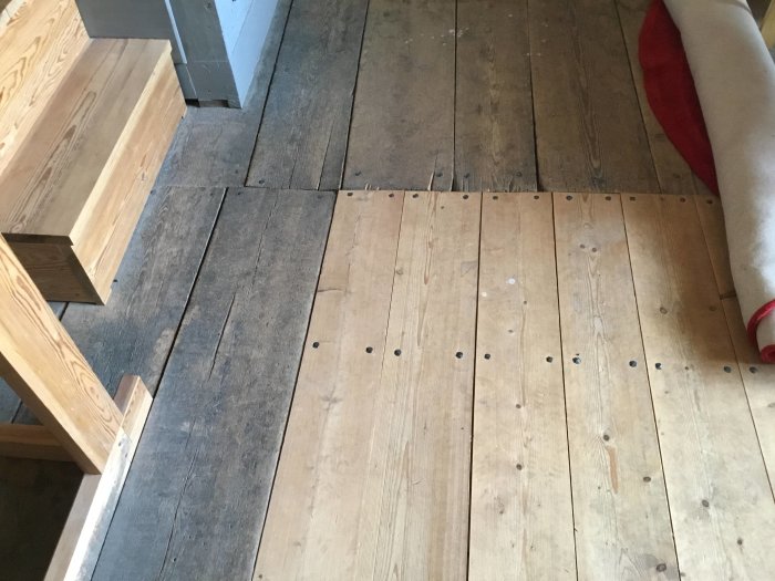 Trägolv med olika åldrar och nyanser i övergång mellan gammalt och nyare trämaterial i en kyrka.