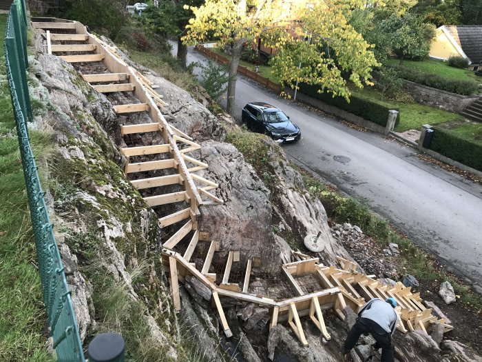 Konstruktion av trätrappa med armering längs ett bergigt landskap, en person arbetar på plats.