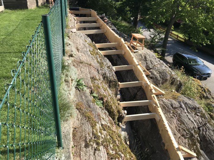 Träformar för en trappa gjutna längs en sluttande bergssida vid sidan av en grön staket.