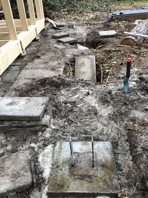 Betongplintar och armeringsjärn i lerig mark vid husgrund i väntan på att stabilisera.