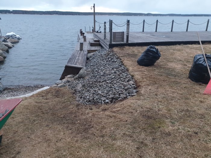 Rensad stenkant vid gräsmatta nära en brygga och sjö, med säckar av trädgårdsavfall.