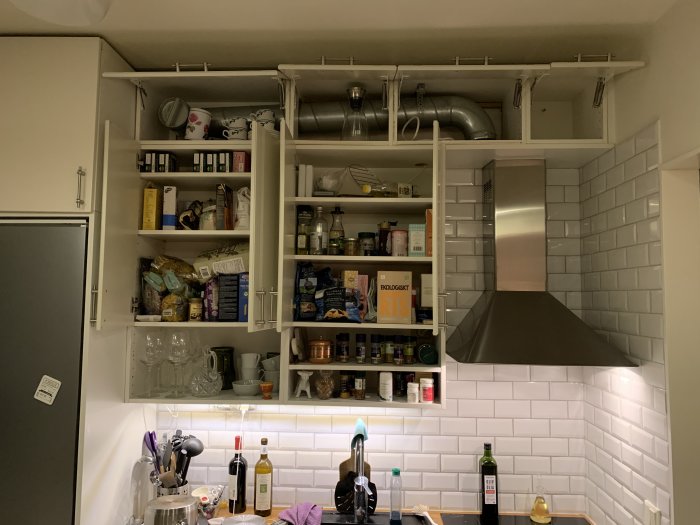 Kök med röriga öppna och saknade köksluckor, exponerade förrådshyllor och synlig köksfläkt.