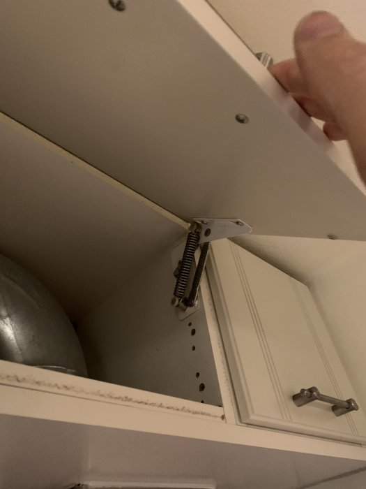 Öppet vit köksskåp med saknade luckor och synliga gångjärn, behöver renovering.
