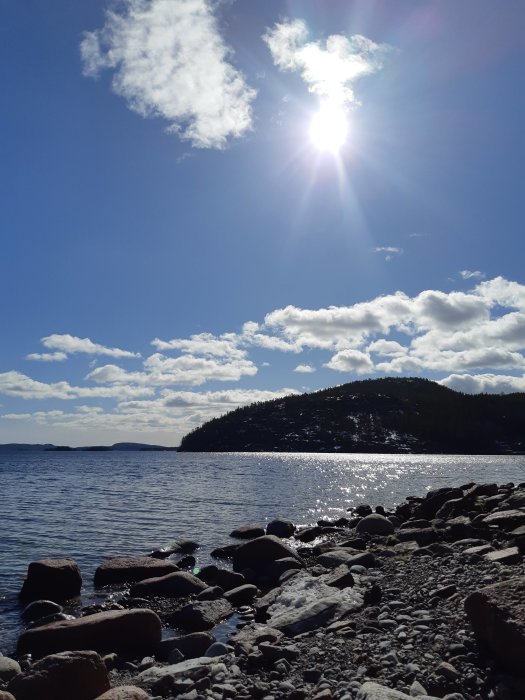 Solig vinterdag vid kusten med snötäckt berg och klippig strand vid Höga kusten.