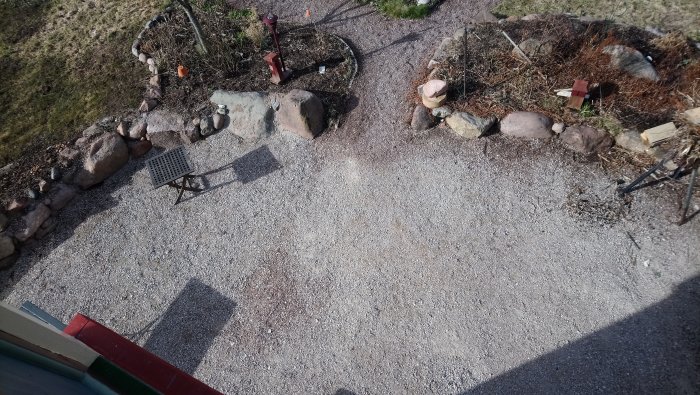 Grusad L-formad uteplats med oregelbunden stensättning i kanten, redo för trallgolvinstallation.