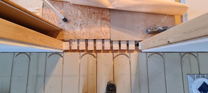 Golvkonstruktion med bjälkar, glespanel, golvvärmeplåtar och början av ett trägolv.