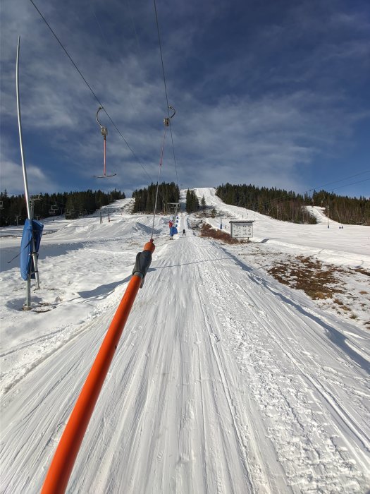 Vy från ett skidlifts stollift med utsikt över en snötäckt backe och skidåkare under en klarblå himmel.