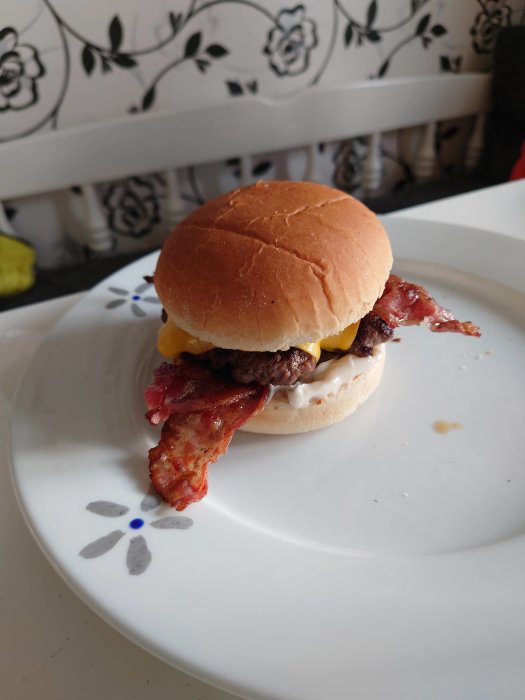 Hamburger med ost och bacon serverad på en vit tallrik mot bakgrund av en köksinredning.