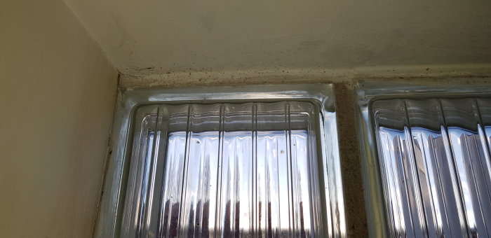 Sovrumsfönster med högt placerade, infällda glasrutor och svarta prickar vid övre karmen som misstänks vara mögel.