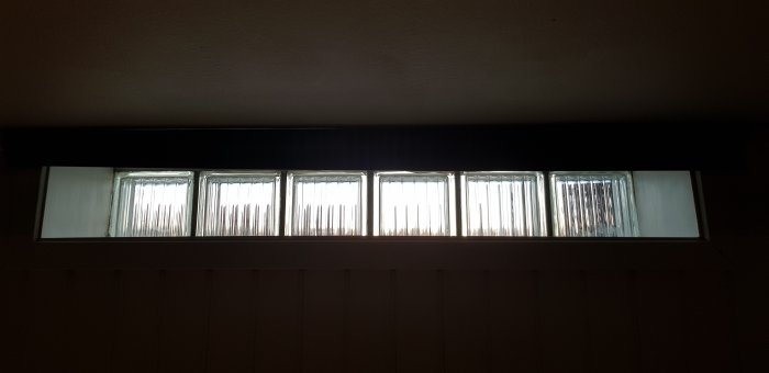 Långt, smalt fönster högt upp på en vägg med svarta prickar som eventuellt är mögel.