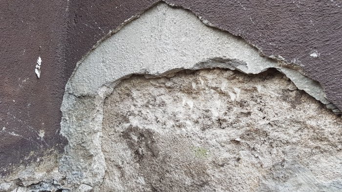 Skadad grund med synliga sprickor och avskalningar på en äldre murad konstruktion.