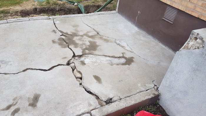 Sprucket betongtrappsteg vid en husgrund med synliga skador och ojämn yta, i behov av reparation.