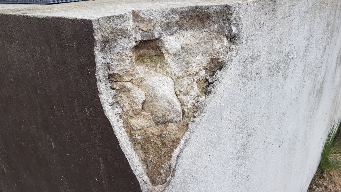 Skadad hörndel av en betonggrund med små sprickor och en stor urgröpning som exponerar sten och gammalt bruk.